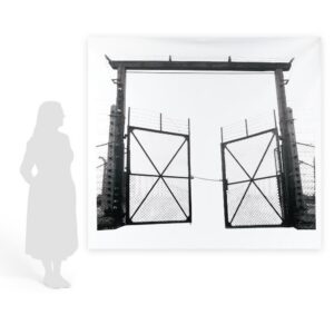 Monumental film negative photograph titled "Barbed Gate" by artist Casey McKee, depicting an inverted light-and-shadow view of the historic gate at the Auschwitz II-Birkenau concentration camp.