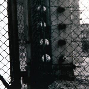 Monumental film negative photograph titled "Barbed Gate" by artist Casey McKee, depicting an inverted light-and-shadow view of the historic gate at the Auschwitz II-Birkenau concentration camp.
