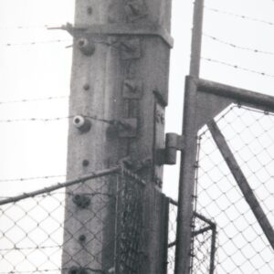 Monumental film negative photograph titled "Barbed Gate" by artist Casey McKee, depicting an inverted light-and-shadow view of the historic gate at the Auschwitz II-Birkenau concentration camp.